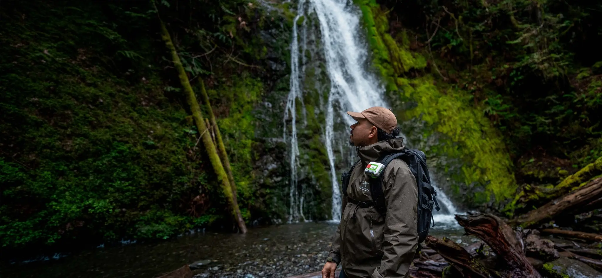A hiker wearing a ZOLEO communicator near a waterfall